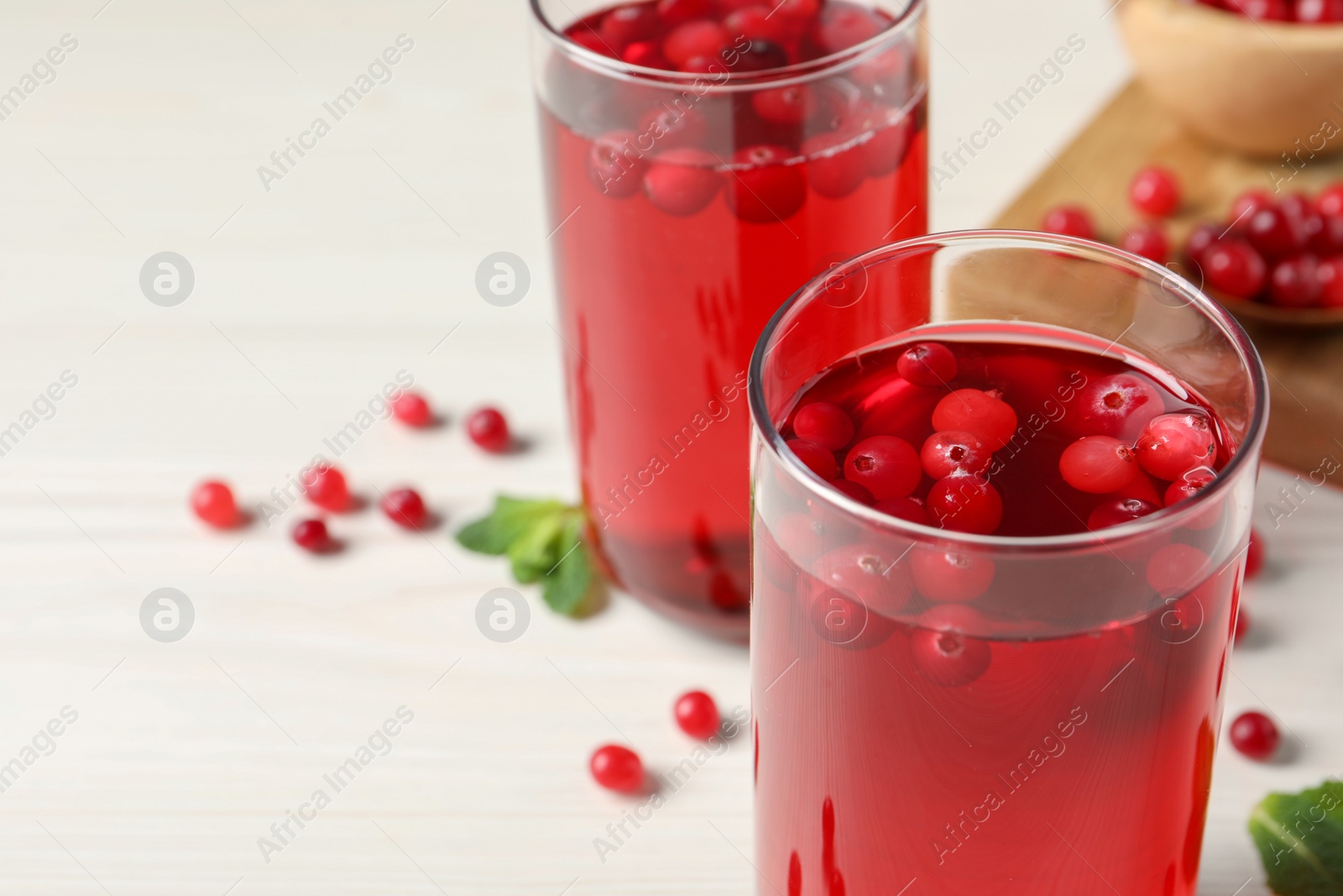 Photo of Tasty cranberry juice in glasses and fresh berries on white wooden table, closeup. Space for text