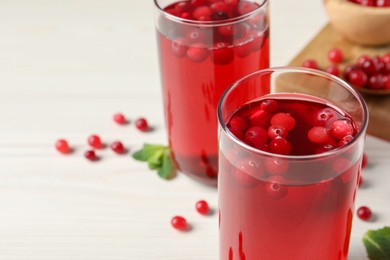 Photo of Tasty cranberry juice in glasses and fresh berries on white wooden table, closeup. Space for text