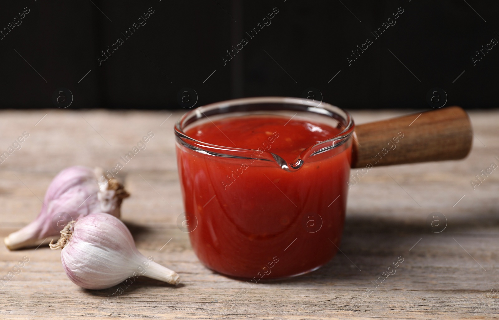 Photo of Delicious ketchup and garlic on wooden table, closeup. Tomato sauce