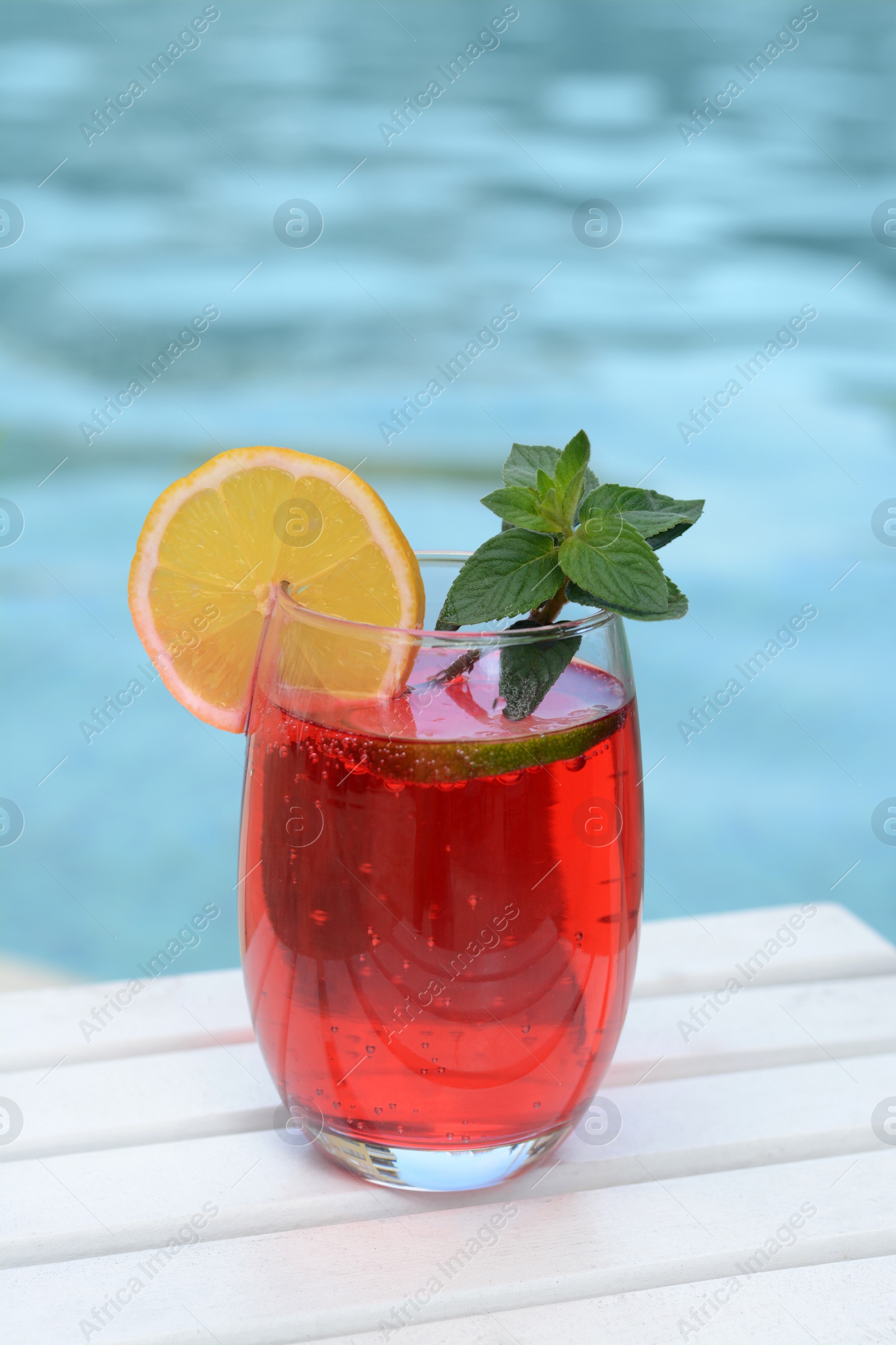 Photo of Glass of delicious cocktail on white wooden table near swimming pool. Refreshing drink