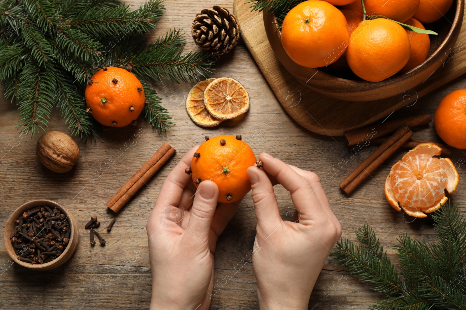 Photo of Woman decorating fresh tangerine with cloves at wooden table, top view. Christmas atmosphere