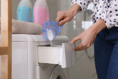 Photo of Woman pouring laundry detergent into washing machine drawer in bathroom, closeup