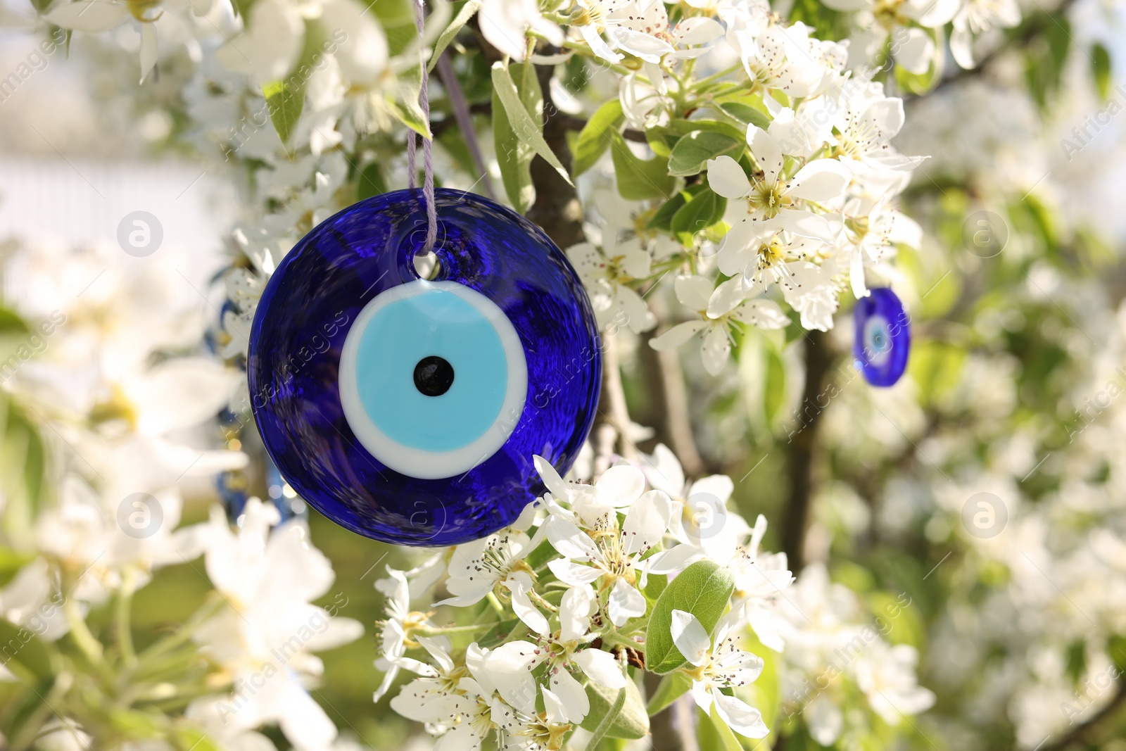 Photo of Eye bead against evil eye hanging on blossoming tree outdoors, closeup