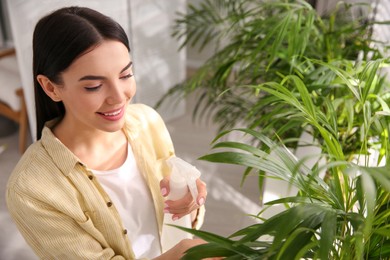 Woman spraying leaves of house plants indoors