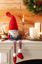 Photo of Cute Christmas gnome and festive decorations on mantelpiece in room