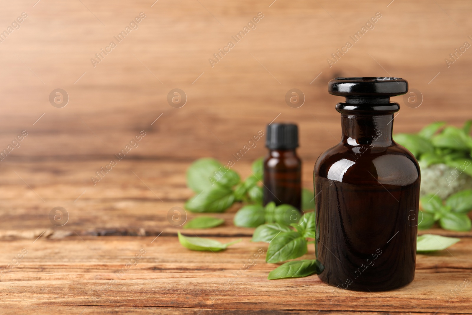 Photo of Glass bottles of basil essential oil and leaves on wooden table, space for text