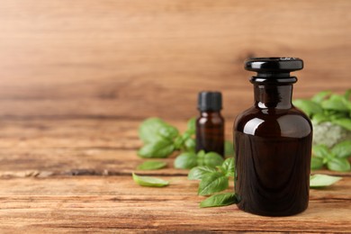 Photo of Glass bottles of basil essential oil and leaves on wooden table, space for text