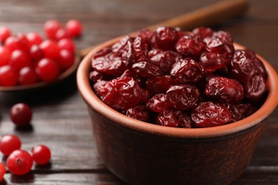 Photo of Tasty dried cranberries in bowl and fresh ones on wooden table, closeup