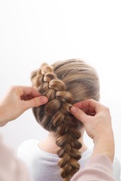 Photo of Professional stylist braiding girl's hair on white background, closeup