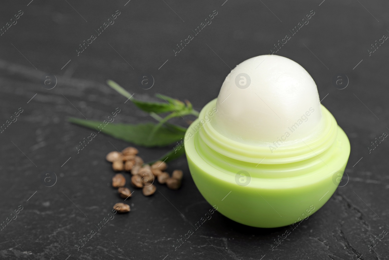 Photo of Lip balm, hemp leaf and seeds on black table, closeup. Natural cosmetics