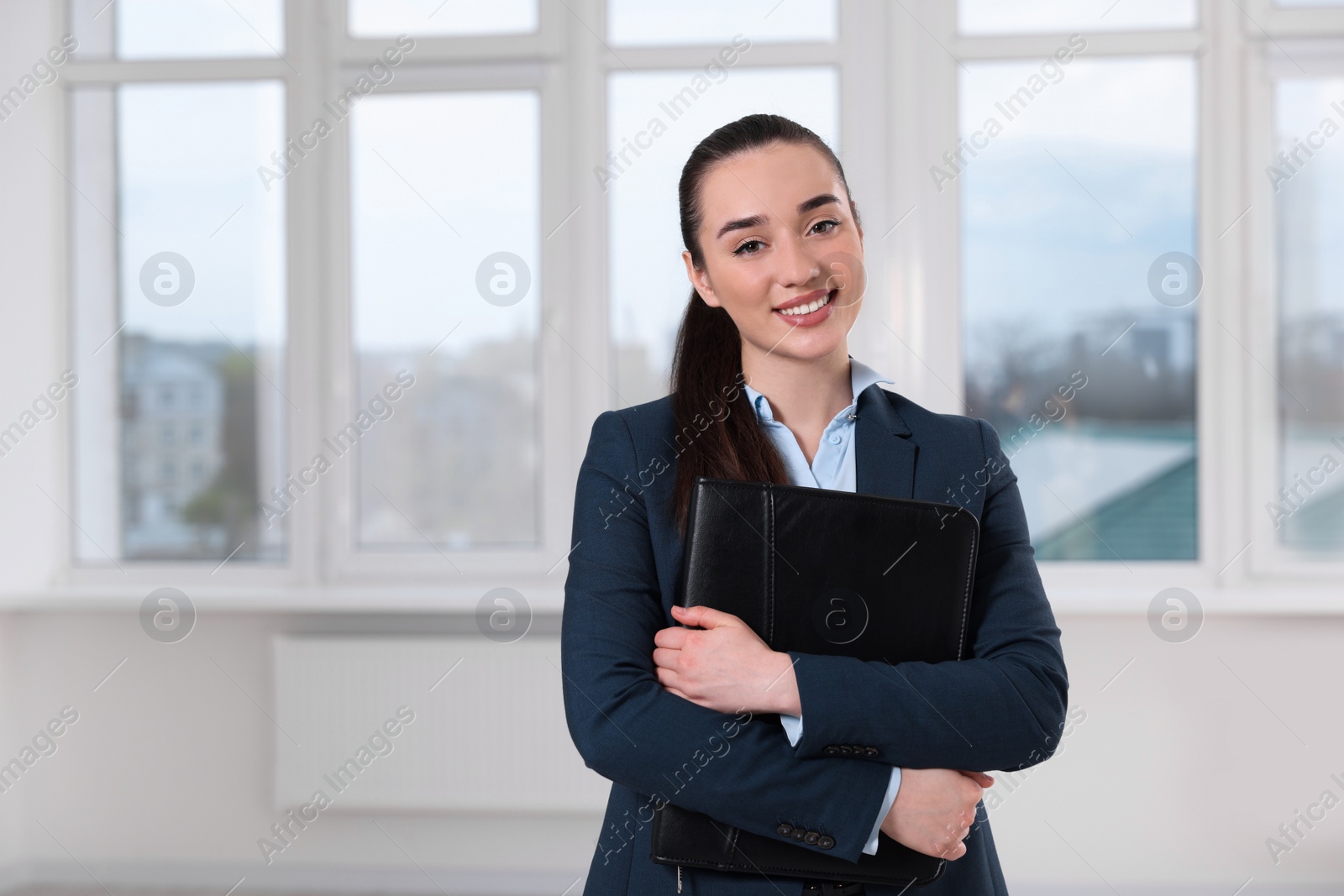 Photo of Happy real estate agent with leather portfolio indoors. Space for text