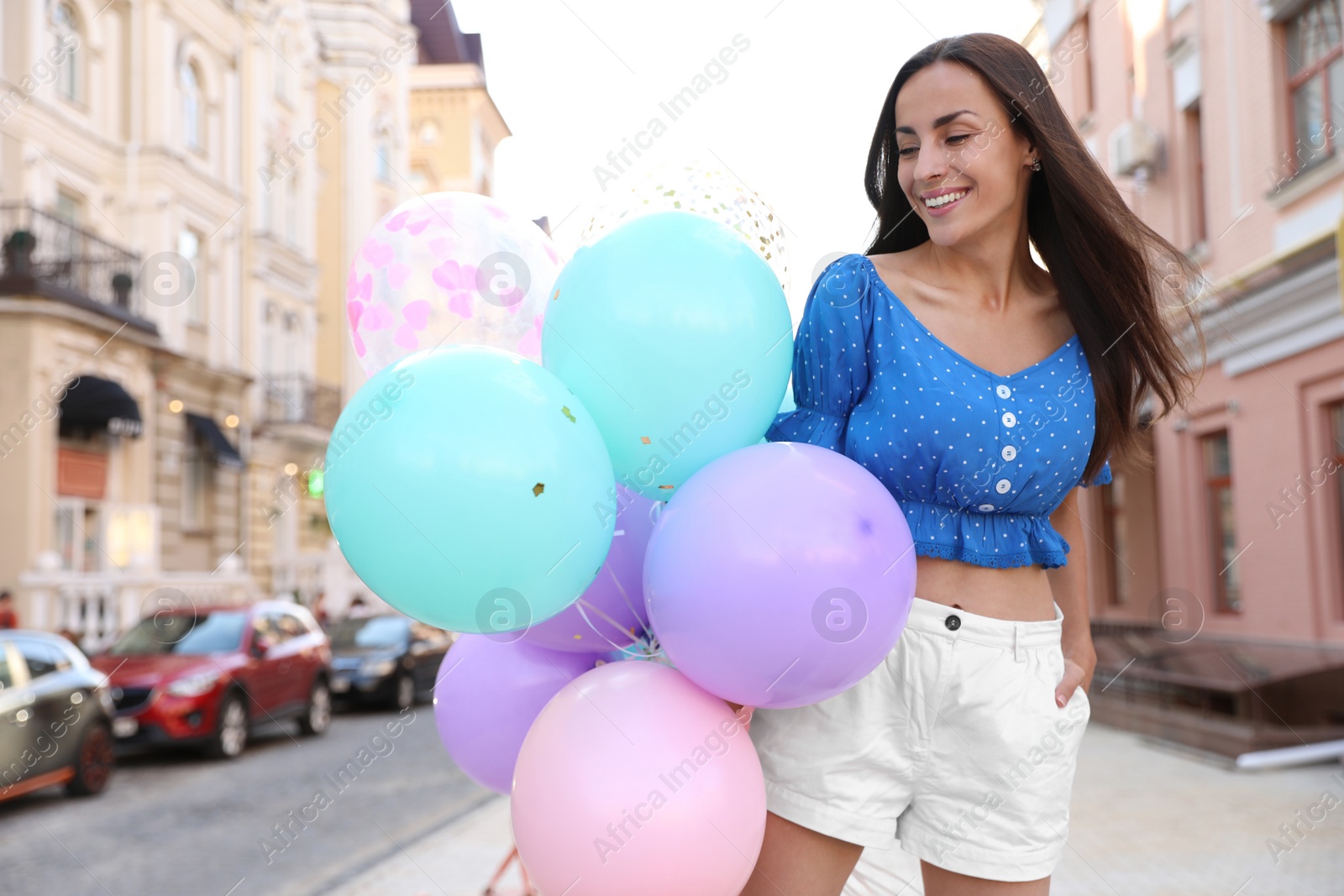 Photo of Beautiful young woman with color balloons on city street