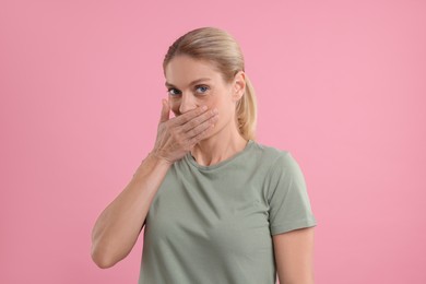 Photo of Portrait of embarrassed woman covering mouth with hand on pink background