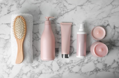Different hair products, towel and brush on white marble table, flat lay