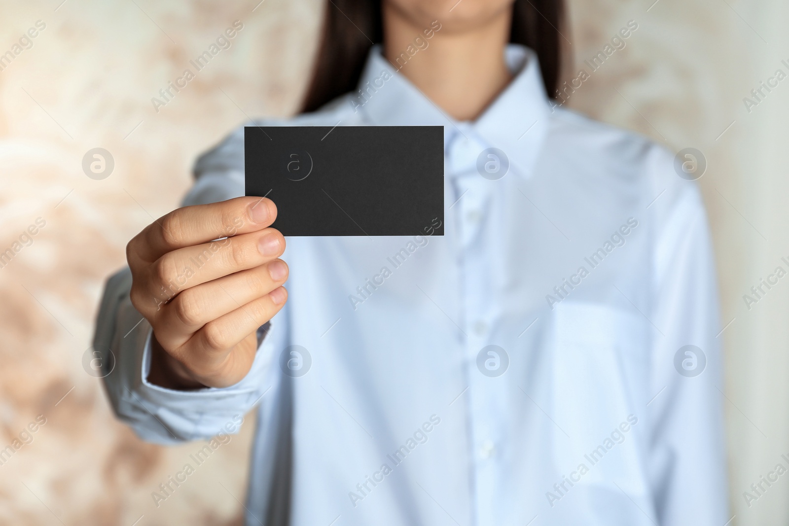 Photo of Woman holding blank business card on blurred background, closeup. Mockup for design