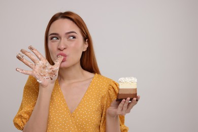 Photo of Young woman eating piece of tasty cake on light grey background, space for text