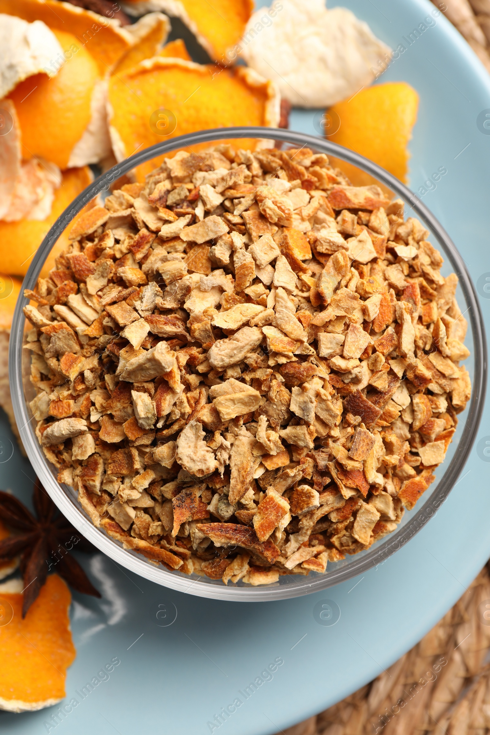 Photo of Bowl of dried orange zest seasoning, fresh peel and anise on wicker mat, flat lay