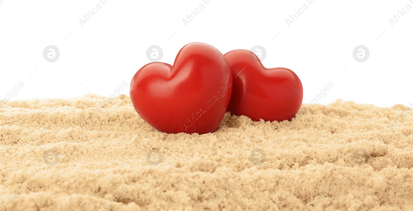 Photo of Honeymoon concept. Two red wooden hearts and sand isolated on white