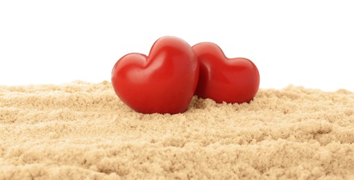 Honeymoon concept. Two red wooden hearts and sand isolated on white