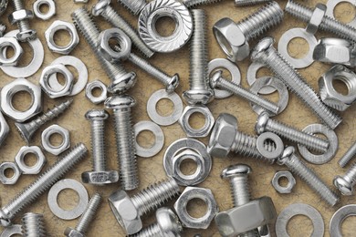 Different metal bolts and nuts on beige textured table, flat lay