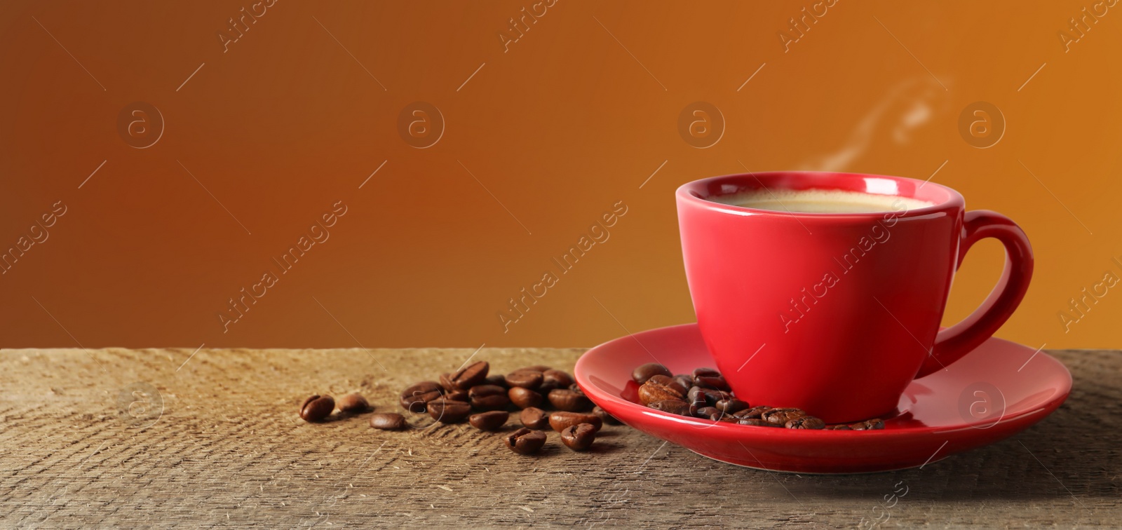 Image of Cup of hot aromatic coffee and roasted beans on wooden table against brown background. Space for text