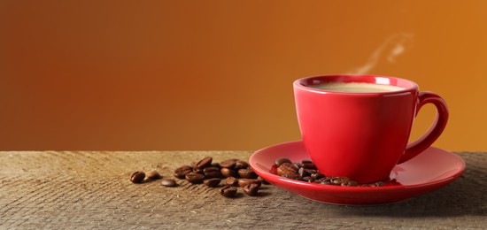 Cup of hot aromatic coffee and roasted beans on wooden table against brown background. Space for text
