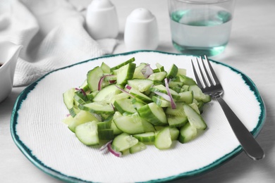 Plate of vegetarian salad with cucumber and onion served on table, closeup