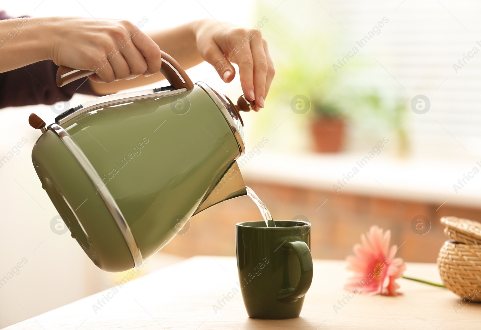 Photo of Woman pouring water into ceramic cup at table indoors, closeup