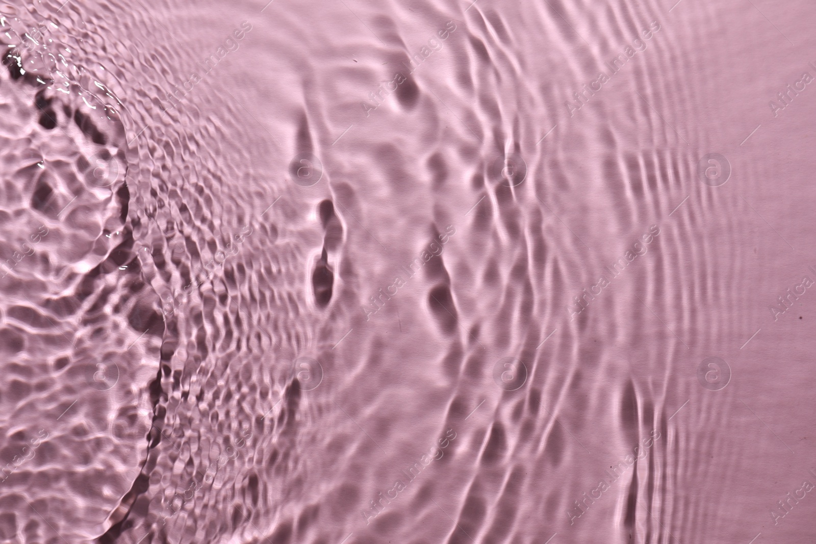 Photo of Rippled surface of clear water on pink background, top view