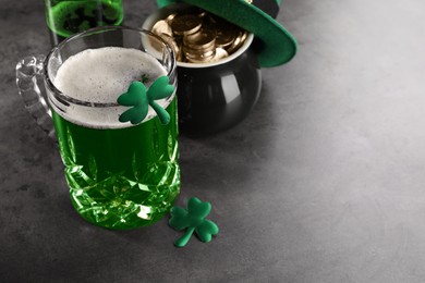 Photo of St. Patrick's day celebration. Green beer, leprechaun hat, pot of gold and decorative clover leaves on grey table. Space for text