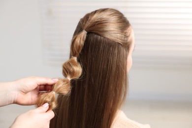 Photo of Professional stylist braiding woman's hair indoors, closeup