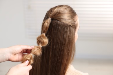 Professional stylist braiding woman's hair indoors, closeup