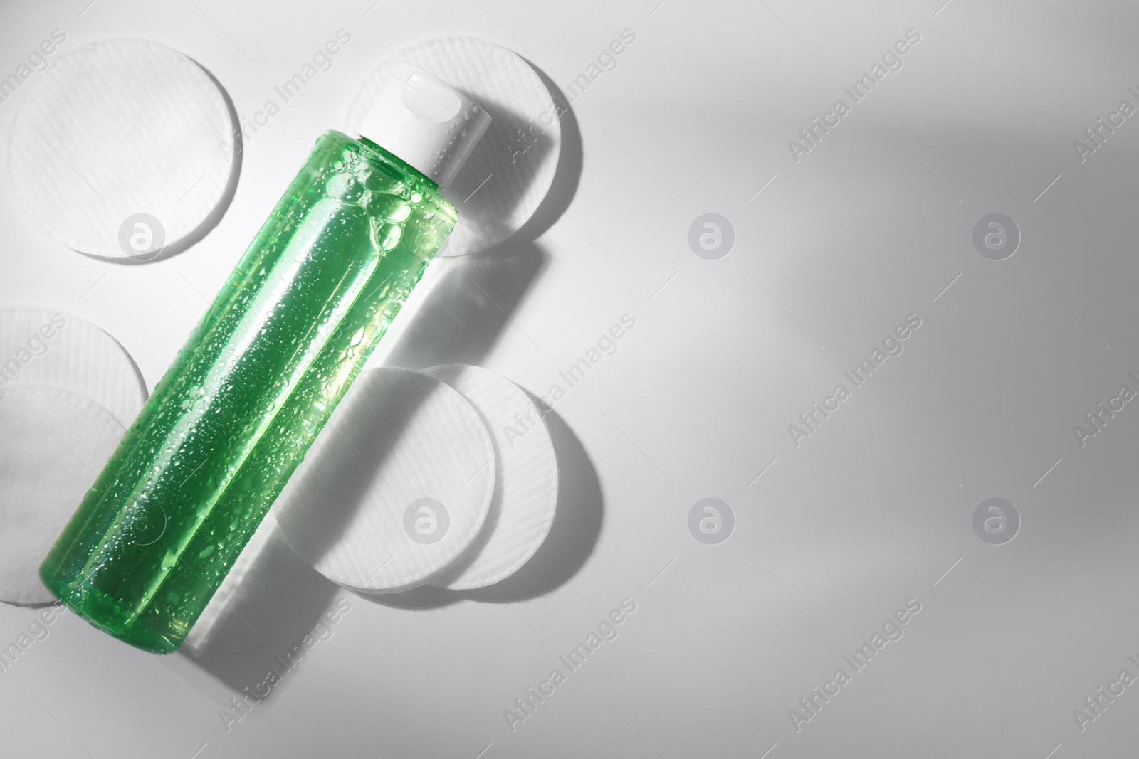 Photo of Wet bottle of micellar water and cotton pads on white background, flat lay. Space for text