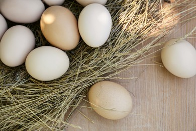 Nest with fresh raw eggs on wooden table, flat lay