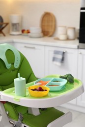 Photo of High chair with food in baby tableware on tray indoors