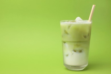 Glass of tasty iced matcha latte on light green background. Space for text