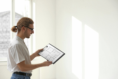 Photo of Professional interior designer with clipboard in empty apartment. Space for text