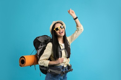 Happy female tourist with backpack on light blue background