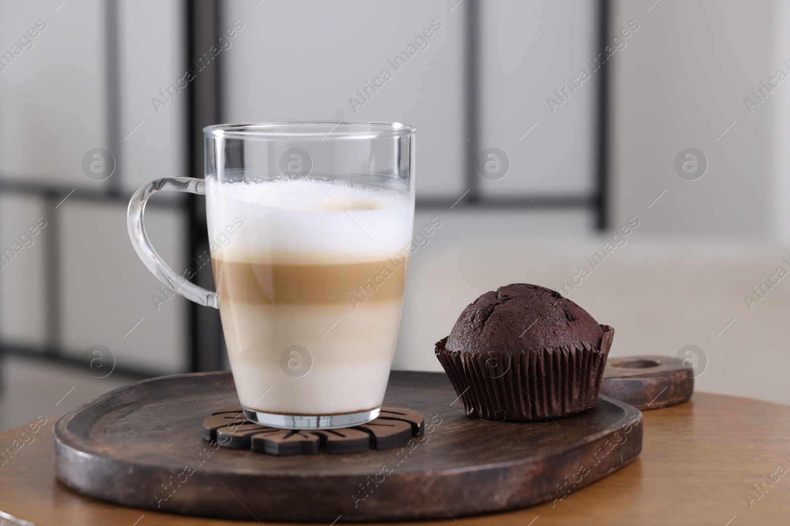 Photo of Cup of aromatic latte macchiato and chocolate muffin on wooden table against blurred background