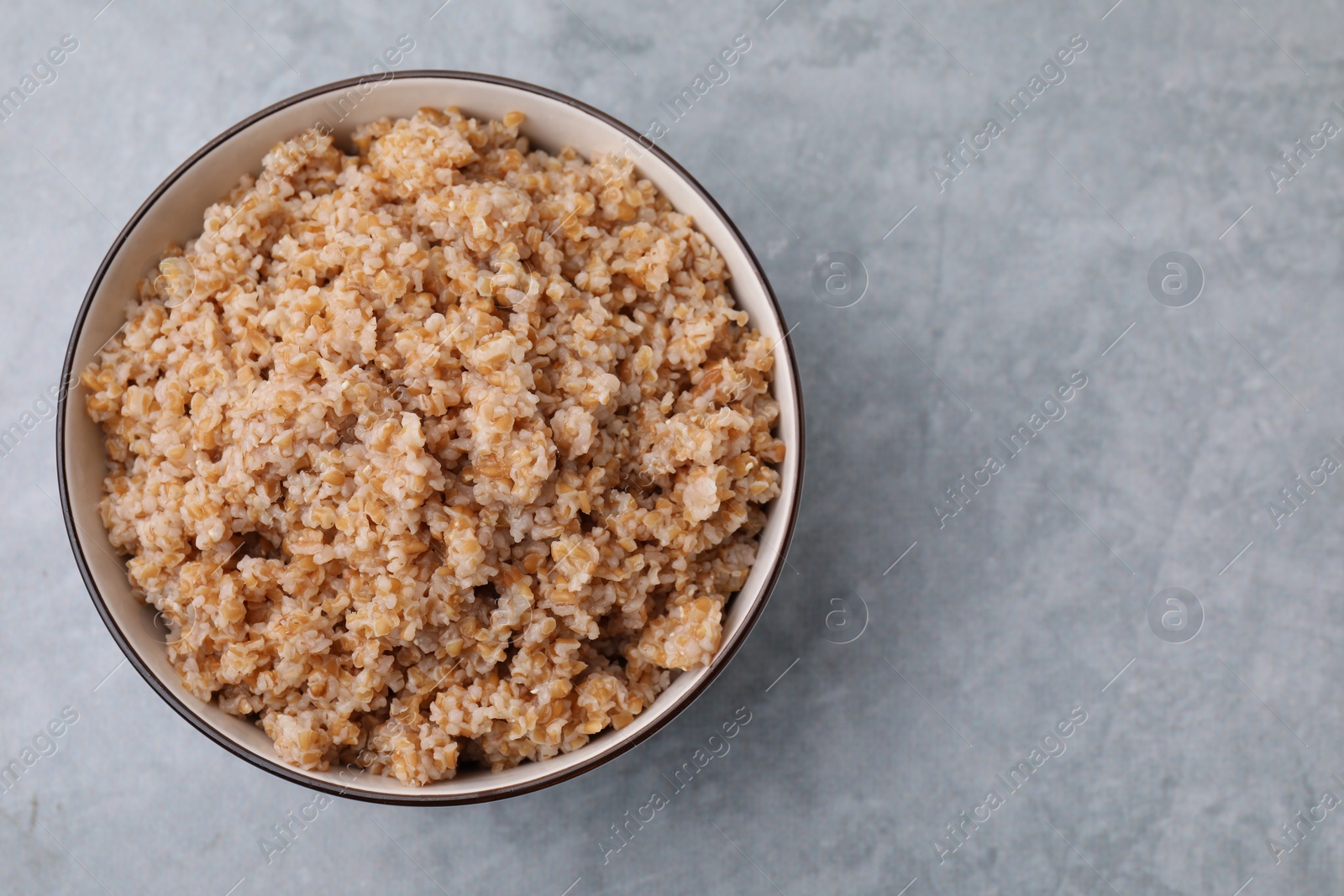 Photo of Tasty wheat porridge in bowl on grey table, top view. Space for text