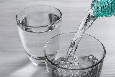 Pouring soda water from bottle into glass on white wooden table, closeup