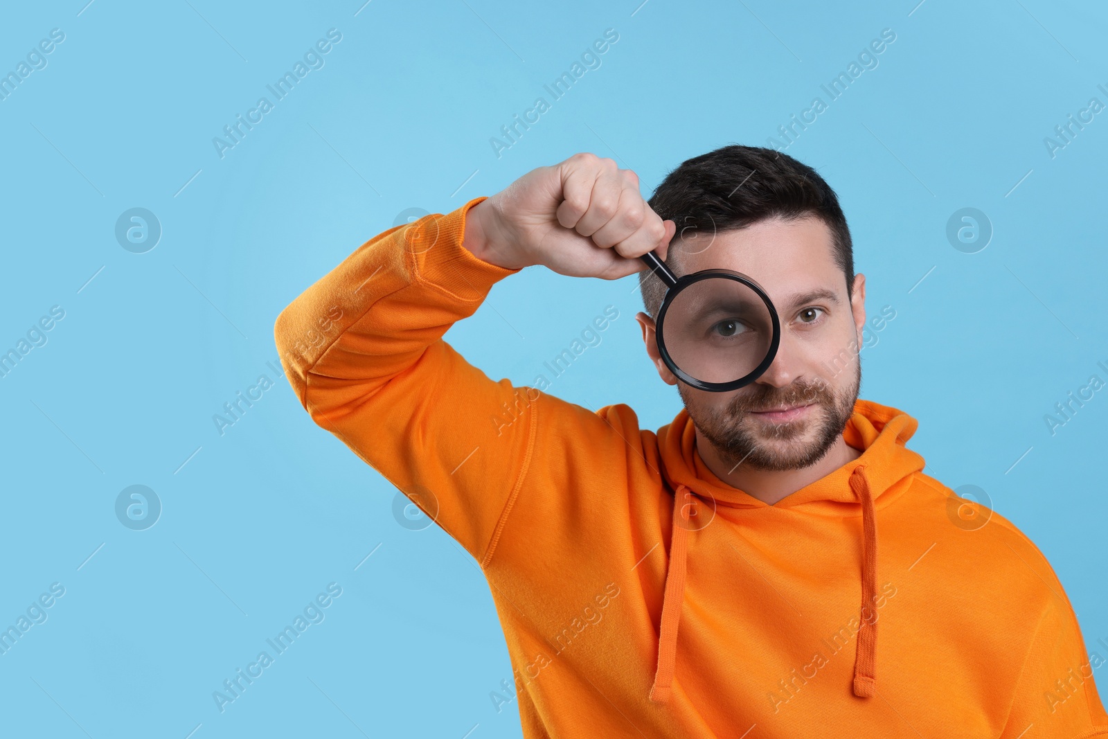Photo of Man looking through magnifier glass on light blue background, space for text