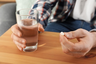 Photo of Man holding pill and glass of water at table, closeup