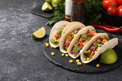 Tasty tacos with vegetables on black textured table, space for text