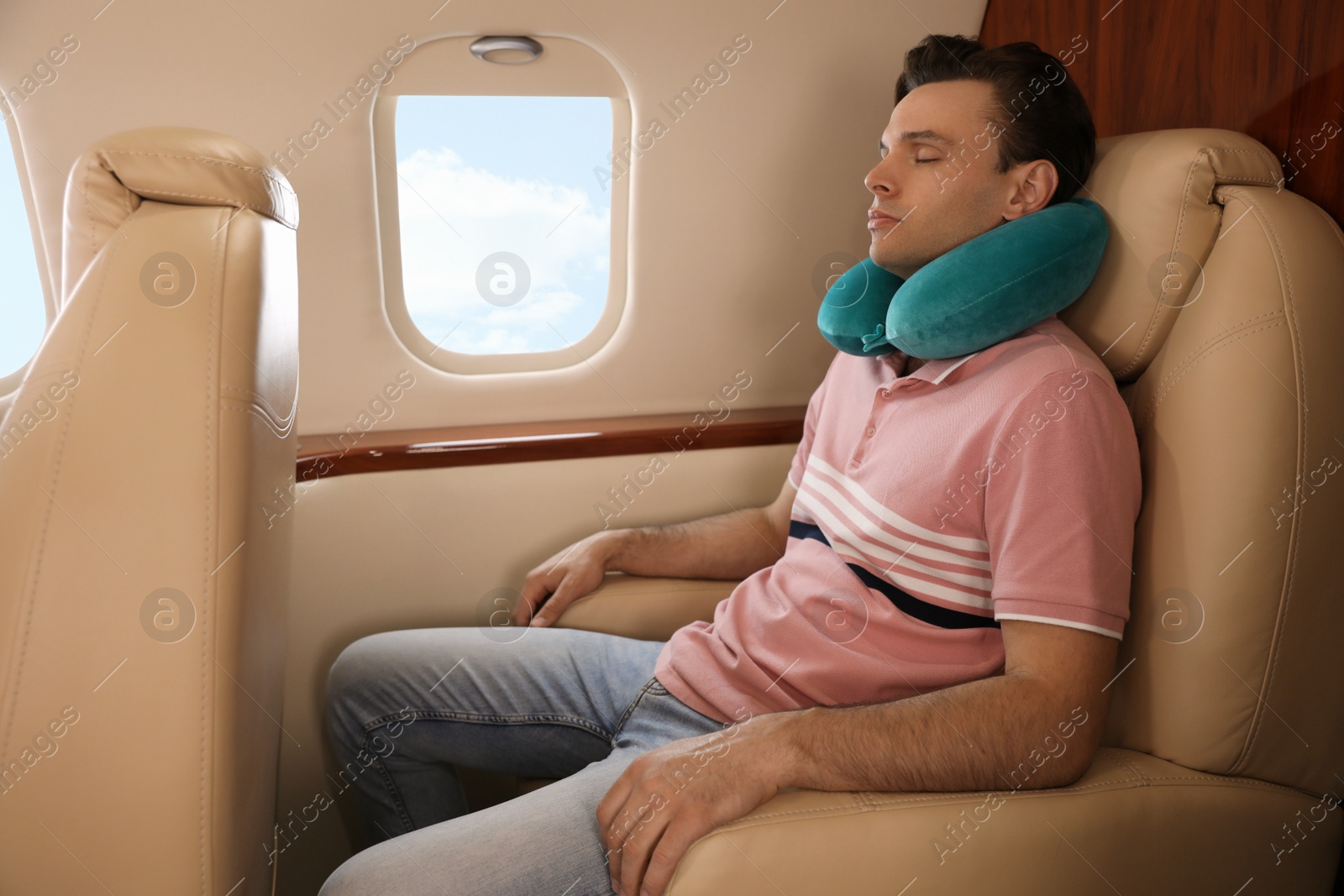 Photo of Young man with travel pillow sleeping in airplane during flight