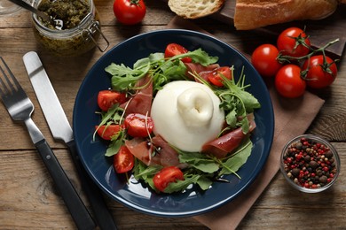 Photo of Delicious burrata salad with tomatoes, prosciutto and arugula served on wooden table, flat lay