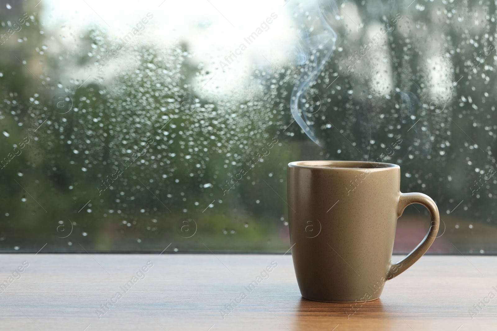 Photo of Cup of hot drink near window on rainy day. Space for text