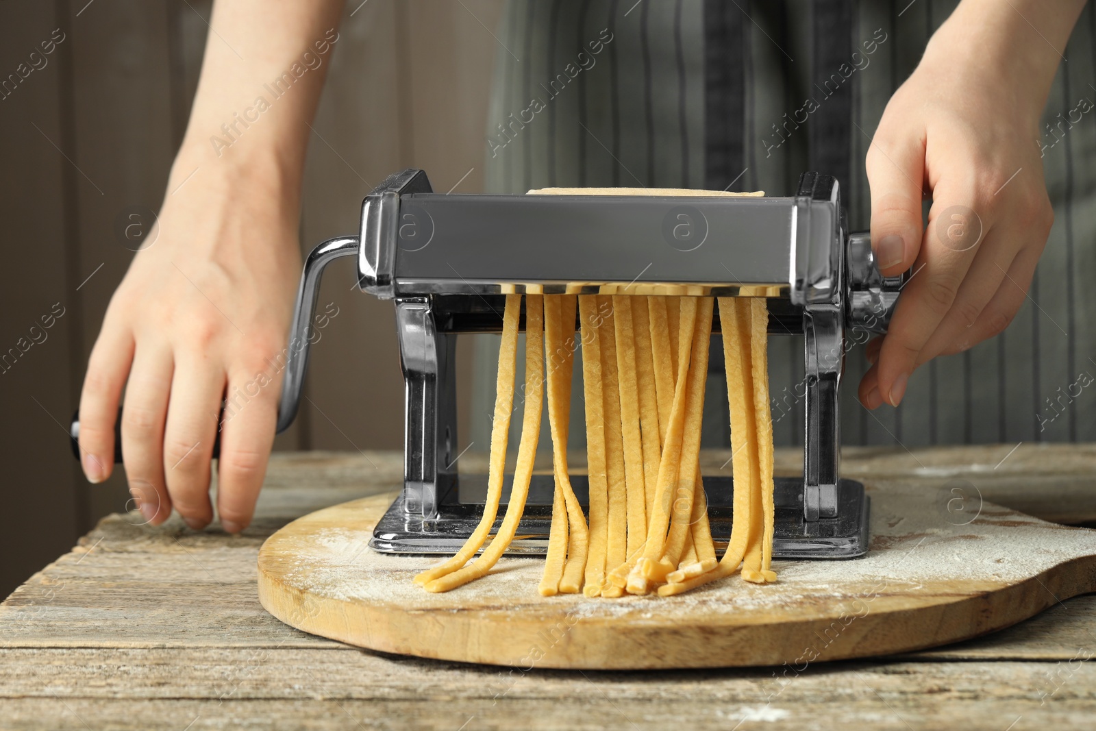 Photo of Woman making homemade noodles with pasta maker at wooden table, closeup