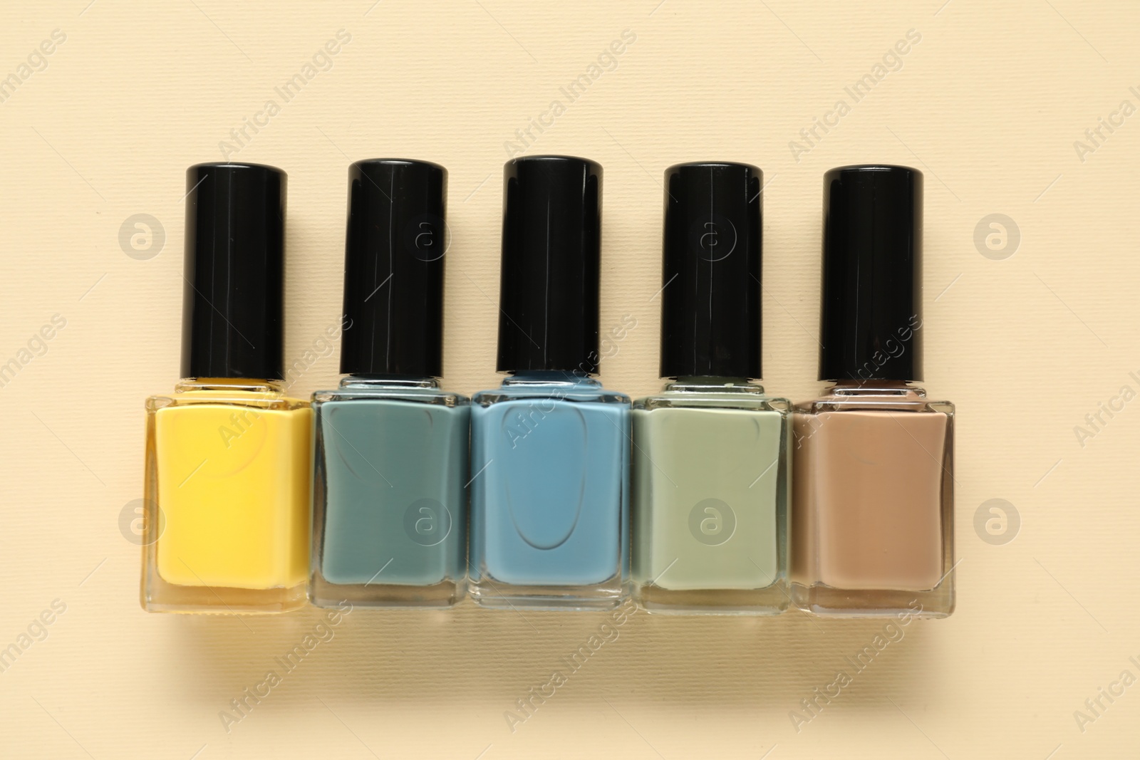 Photo of Bright nail polishes in bottles on beige background, flat lay