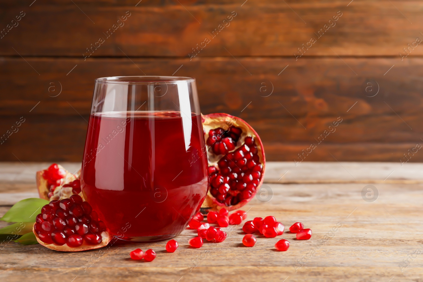 Photo of Glass of pomegranate juice and fresh fruits on table against wooden background, space for text